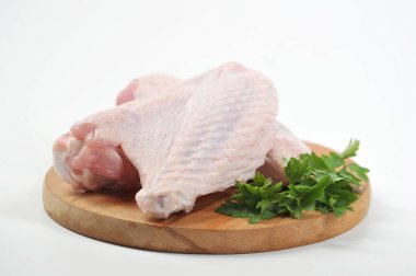 Yuvarlak tahta bir tahta üzerinde hindinin iki kanadı. Hindinin yanındaki tahtada maydanozun yeşili yatıyor. Beyaz arka plan. Close.