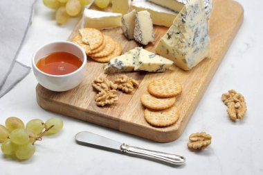 Hafif bir arka plan üzerinde peynir tabağı. Küf dorblu ile peynir ahşap bir tabak dilimleri üzerinde, kül, brie, yeşil üzüm, kraker, bal ve ceviz camembert. Close.