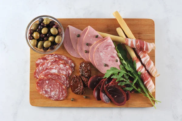 Tahta tepside, etli atıştırmalık. Haşlanmış dana sosisi, salchichen, kurutulmuş sığır-basturma, domuz pastırmalı grissini-breadsticks. Çerçevede, kurutulmuş domates, arugula, kapari, zeytin. Yukarıdan görüntüleyin. Close.