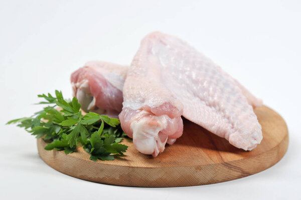 Two wings of turkey on a round wooden board. On the board next to the turkey lies the green of parsley. White background. Close-up.