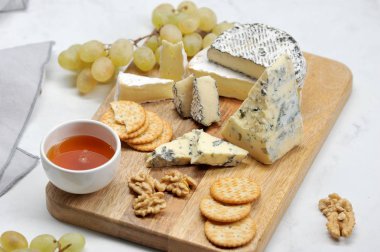 Hafif bir arka plan üzerinde peynir tabağı. Küf dorblu ile peynir ahşap bir tabak dilimleri üzerinde, kül, brie, yeşil üzüm, kraker, bal ve ceviz camembert. Close.