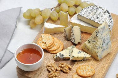 Hafif bir arka plan üzerinde peynir tabağı. Küf dorblu ile peynir bir tabak üzerinde, kül, brie, yeşil üzüm, kraker, bal ve ceviz camembert. Close. Makro fotoğrafçılık.