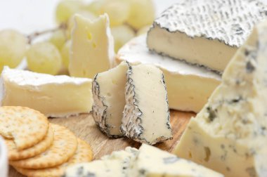 Peynir tabağı: küf lü peynir dorblu, kraker, üzüm, camembert külleri, hafif ahşap tahta üzerinde brie. Beyaz arka plan. Close. Makro fotoğrafçılık.