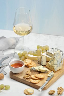 Peynir ile kalıp, kraker, üzüm, bal, brie, camembert hafif ahşap tahta üzerinde. Çerçevede, bir peçete, bir kadeh şarap ve peynir için bir bıçak. Açık arka plan. Close. Dikey yönlendirme.