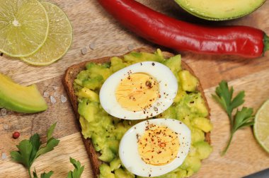 Avokado ve haşlanmış yumurta iki yarısı ile tost. Çerçeveiçinde, avokado dilimleri, kireç ve kırmızı biber biber. Açık ahşap arka plan. Close. Yukarıdan görüntüle.