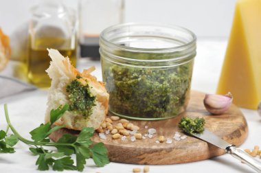 Bir kavanozda yeşil pesto sosu, büyük tuz, sarımsak karanfil, ahşap bir tabakta çam fıstığı. Çerçevede, bir parça Parmesan peyniri, zeytinyağı, bir dilim ciabatta. Close. Makro fotoğrafçılık.