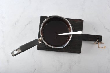 Bir kepçede eritilmiş koyu çikolata. Kepçe ahşap bir tahta üzerinde yer almaktadır. Açık mermer arka plan. Yukarıdan görüntüleyin. Close.