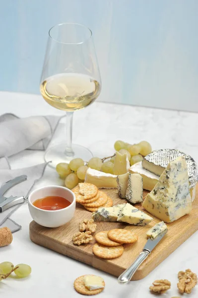 Peynir ile kalıp, kraker, üzüm, bal, brie, camembert hafif ahşap tahta üzerinde. Çerçevede, bir peçete, bir kadeh şarap ve peynir için bir bıçak. Açık arka plan. Close. Dikey yönlendirme.