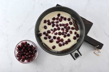 Hamur pişirme şeklinde. Üstüne bisküvisüz peynir hamuru ve vişne böğürtlenleri. Kirazlı kasenin yanında. Açık mermer arka plan. Close. Yukarıdan görüntüle.