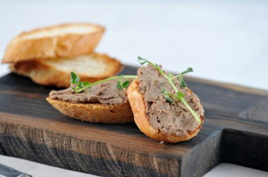 Kızarmış beyaz ekmek dilimleri üzerinde karaciğer pate. Sandviçler genç bezelye dalları ile dekore edilmiştir. Çerçevede ahşap bir tahta ve baget dilimleri bulunmaktadır. Açık arka plan. Close. Makro fotoğrafçılık.