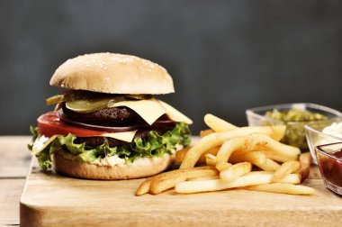 Hafif ahşap bir masada çift çizburger ve patates kızartması. Burger dolgu iki biftek, sebze, peynir ve sos oluşur. Karanlık arka plan. Close.