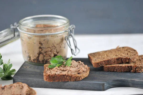 Tahta bir tahtada, ciğer pate ile siyah ekmek birkaç dilim. Pate ile cam bir kavanoz yanında. Close. Makro fotoğrafçılık.