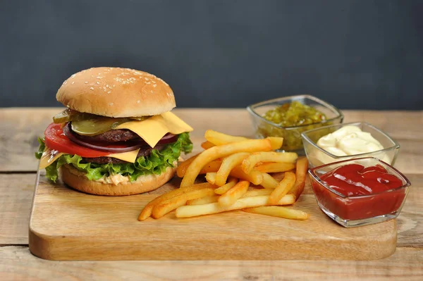 Çifte çizburger ve patates kızartması. Burger dolgu iki biftek, sebze, peynir ve sos oluşur. Soslu patates kasesi yanında. Close. Koyu arka plan.