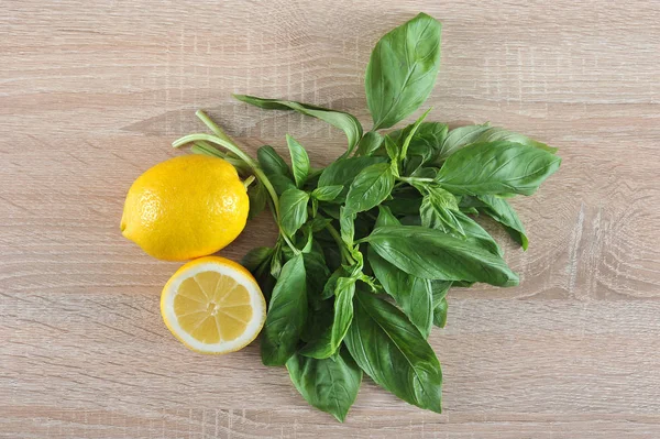 The greens of the basil are a bunch, half a lemon and a whole lemon. Light wooden background. View from above. Close-up. Macro photography.