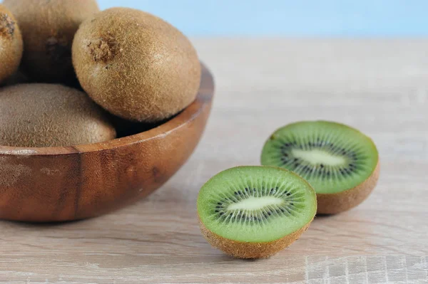 Yuvarlak ahşap bir kapta olgun kivi. Kabın yanında kivi var, ikiye bölünüyor. Açık ahşap arka plan. Close. Makro fotoğrafçılık.