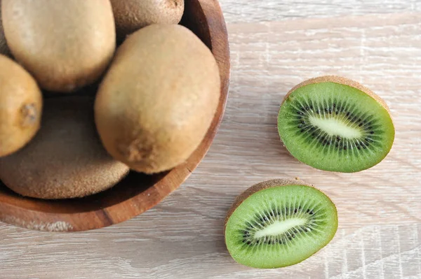 Yuvarlak ahşap bir kapta olgun kivi. Kabın yanında kivi var, ikiye bölünüyor. Açık ahşap arka plan. Yukarıdan görüntüleyin. Close. Makro fotoğrafçılık.