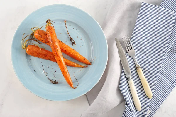 Mavi tabakta bal ve baharatla pişirilen havuçlar. Yemeğin yanında bez peçete ve çatal bıçak takımı var. Açık arka plan. Yukarıdan görüntüleyin. Close.