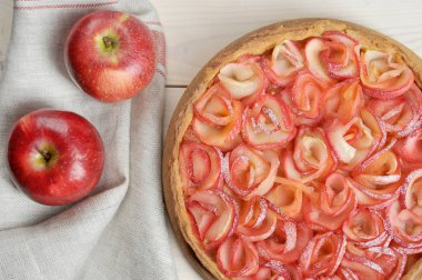 Elmalı turta. Pastanın açık kısmı gül şeklinde serilmiş elma parçaları ile süslenir. Pasta bezi peçeteleri ve elmaların yanında. Açık ahşap arka plan. Close. Yukarıdan görüntüle.