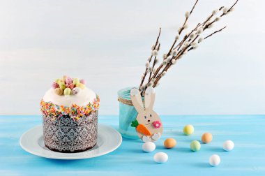 Tabakta Paskalya pastası. Söğüt dalları olan vazonun yanında. Yumurta şeklinde tatlılar yüzeye yayılır. Çerçevede bir tavşan ahşap bir rakamdır. Açık arka plan. Close.