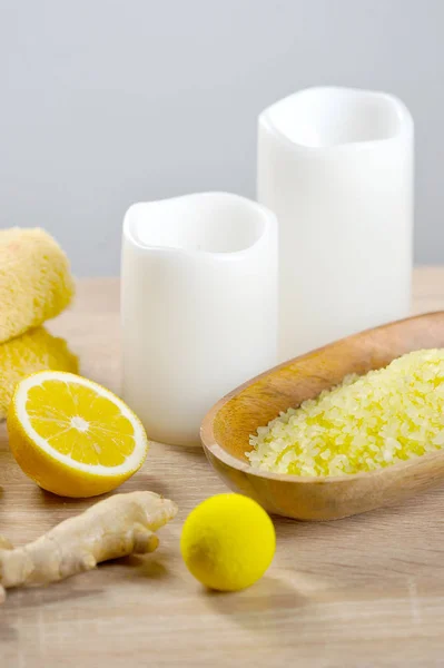 Lemon-ginger body scrub and bath salt for body cleansing and toning procedures. The composition is complemented by candles, half a lemon and ginger root. Light background. Close-up. Vertical frame.