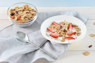 Bir tabakta yoğurtlu mısır gevreği. Pullar için kurutulmuş meyve ve taze çilek eklendi. Bardaka yakın, pullarla. Çerçevede, bir peçete ve bir kaşık var. Açık arka plan. Close.
