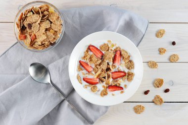 Bir tabakta yoğurtlu mısır gevreği. Pullar için kurutulmuş meyve ve çilek eklendi. Bardaka yakın, pullarla. Çerçevede, bir peçete ve bir kaşık var. Açık arka plan. Close. Yukarıdan görüntüle.