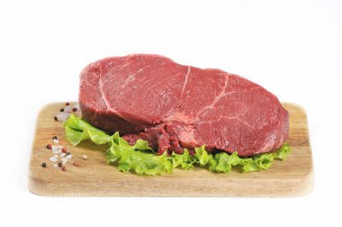 Tahta tahtada bir dilim çiğ sığır eti. Et yeşil marul ve baharat yaprakları ile dekore edilmiştir. Beyaz arka plan. Close.
