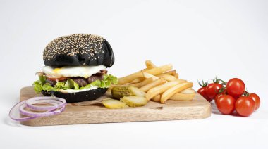 Hafif ahşap tahtada siyah burger. Dolgu köfte, kızarmış yumurta, sos, sebze oluşur. Hamburger kızartmasının yanında. Arka planda bir kiraz domates dalı. Açık arka plan. 