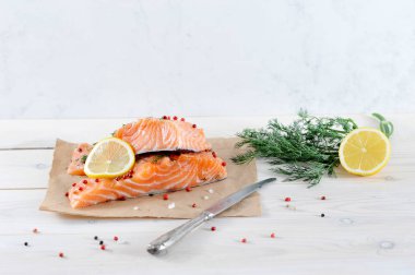 Kraft kağıda iki parça zayıf tuz somon. Bir sürü yeşillik, yarım limon ve bir bıçak var. Açık ahşap arka plan. Close.