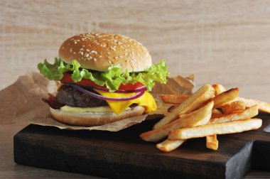 Domates, salata, pastırma, peynir, sos ve soğan ile kıyma köftesi ile Hamburger. Hamburgerin yanında patates kızartması var. Close. Açık arka plan. Makro fotoğrafçılık.