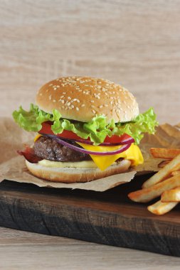 Domates, salata, pastırma, peynir, sos ve soğan ile kıyma köftesi ile Hamburger. Hamburgerin yanında patates kızartması var. Close. Açık arka plan. Çerçevenin dikey yönü.