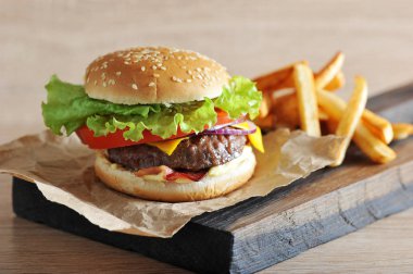 Domates, salata, pastırma, sos ve kırmızı soğan ile doğranmış sığır pirzonu cheeseburger. Çizburgerin yanında patates kızartması var. Açık arka plan. Close. Makro fotoğrafçılık.