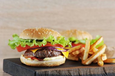 Domates, salata, pastırma, sos ve kırmızı soğan ile doğranmış sığır pirzonu cheeseburger. Çizburgerin yanında patates kızartması var. Arka planda başka bir çizburger olduğunu. Açık arka plan. Close. 