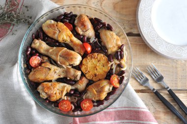 Derin bir cam çanak fasulye ve domates ile Tavuk. Bir sonraki çatal bıçak takımı ve tabaklar. Çerçeve peçete bezyapılmış. Ahşap arka plan. Close. Yukarıdan görüntüle.