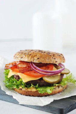 Sulu sığır pirzolası ile cheeseburger. Dolgu kızarmış pastırma dilimleri oluşur. Çörek susam serpilir. Açık arka plan. Close. Çerçevenin dikey yönü. 