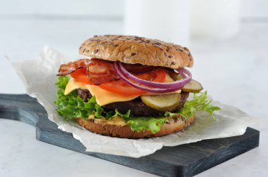 Tahta bir tahtaüzerinde sulu sığır pirzolası ile Cheeseburger. Dolgu kızarmış pastırma dilimleri oluşur. Çörek susam serpilir. Açık arka plan. Close. 