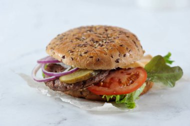 Sulu sığır pirzolası ile cheeseburger. Dolgu salatalık turşusu, kırmızı soğan, domates dilimi, peynir, marul yaprakları ve sos oluşur. Çörek susam serpilir. Açık arka plan.