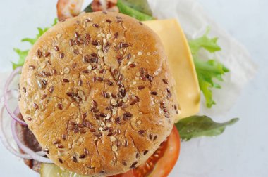 Cheeseburger hafif bir arka plan, üst görünümü. Topuzun beyaz ve siyah susam serpilir. Pirzama, soğan, pastırma, domates, peynir ve marul bir hamburger yaprakları. Close. Makro fotoğrafçılık. 