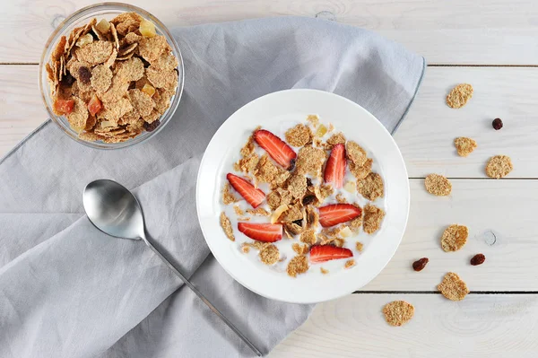 Bir tabakta yoğurtlu mısır gevreği. Pullar için kurutulmuş meyve ve çilek eklendi. Bardaka yakın, pullarla. Çerçevede, bir peçete ve bir kaşık var. Açık arka plan. Close. Yukarıdan görüntüle.