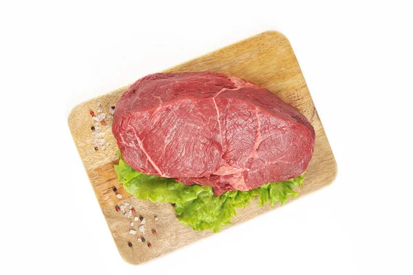 Tahta bir tahtada bir dilim çiğ dana eti. Et yeşil salata ve baharat bir yaprak ile dekore edilmiştir. Beyaz arka plan. Close. Yukarıdan görüntüle.