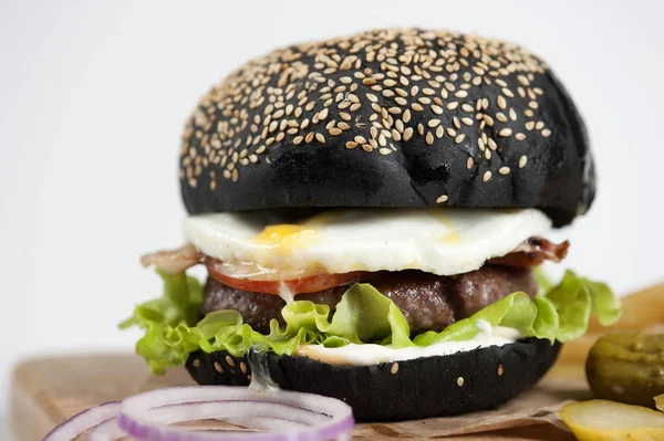 Hafif ahşap tahtada siyah burger. Dolgu köfte, kızarmış yumurta, sos ve sebze oluşur. Açık arka plan. Close. Makro çekimi.