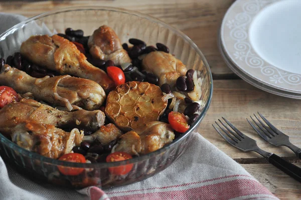 Derin bir cam çanak fasulye ve domates ile Tavuk. Bir sonraki çatal bıçak takımı ve tabaklar. Çerçeve peçete bezyapılmış. Ahşap arka plan. Close. 