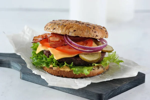 Tahta bir tahtaüzerinde sulu sığır pirzolası ile Cheeseburger. Dolgu kızarmış pastırma dilimleri oluşur. Çörek susam serpilir. Açık arka plan. Close. 