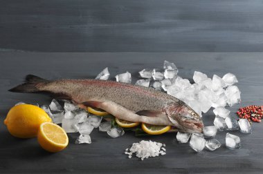 Somon Atlantik çiğ, harcanmış. Balığın karnı limon dilimleri ile doldurulr. Doğal buz, baharat, deniz tuzu küpleri etrafında. Koyu ahşap arka plan. Close.