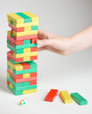 Bulmaca Kulesi. Çok renkli ahşap çubuklar kulesi. Çocuğun eli parmaklıkları kuleden çıkarır. Beyaz arka plan. Close. Dikey çerçeve yönlendirmesi.