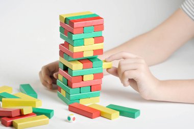 Bulmaca Kulesi. Çok renkli ahşap çubuklar kulesi. Çocuğun eli parmaklıkları kuleden çıkarır. Beyaz arka plan. Close.