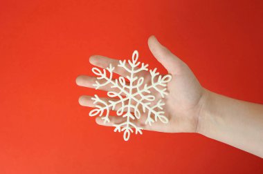 Bir çocuğun avucunda plastikten yapılmış kar tanesi. Close. Kırmızı arka plan. Yukarıdan görüntüle. 