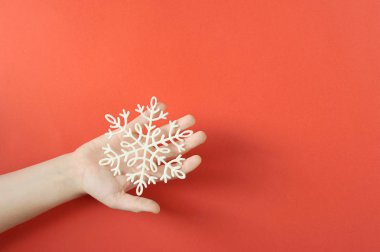 Bir çocuğun avucunda plastikten yapılmış kar tanesi. Close. Kırmızı arka plan. Yukarıdan görüntüleyin. Metin için boş alan.