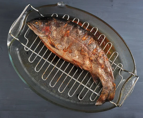 Izgarada pişirilmiş kafası olan Atlantik somonu. Balık ızgara üzerinde bir cam çanak bulunmaktadır. Koyu ahşap arka plan. Yukarıdan görüntüleyin. Close. 