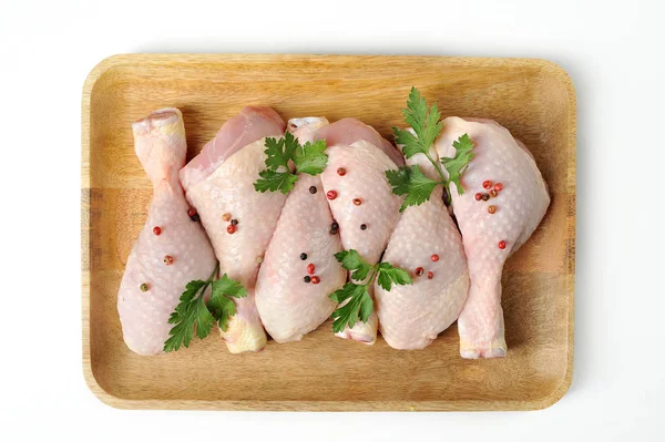 Hafif ahşap tepside çiğ tavuk baget. Tavuk bacakları maydanoz ve baharatlarla süslenmiştir. Beyaz arka plan. Yukarıdan görüntüleyin. Close.